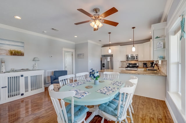 dining space with ceiling fan, sink, ornamental molding, and light wood-type flooring