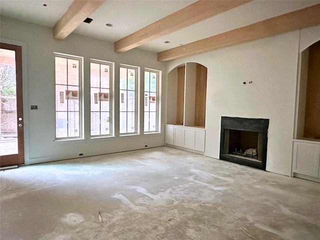 unfurnished living room featuring plenty of natural light, beam ceiling, a fireplace, and concrete floors