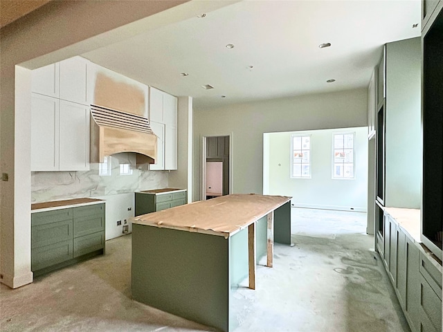 kitchen with unfinished concrete flooring, backsplash, green cabinets, white cabinetry, and a kitchen island