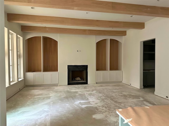 unfurnished living room featuring a fireplace, beamed ceiling, and unfinished concrete floors