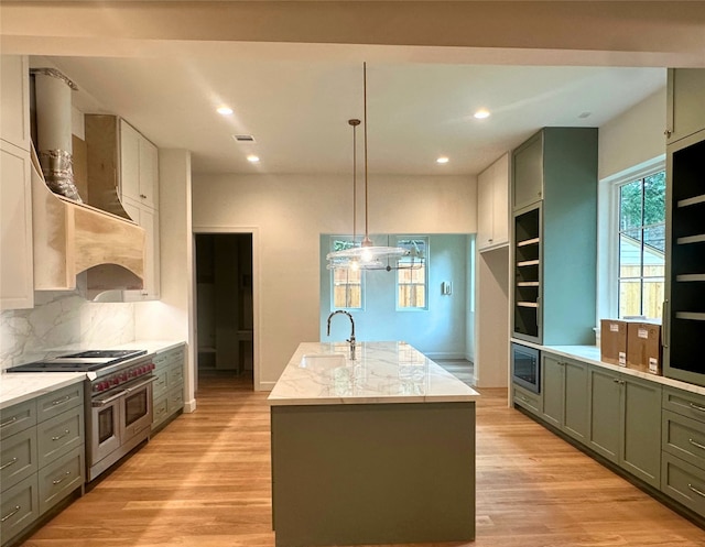 kitchen featuring light stone countertops, a center island with sink, wall chimney range hood, a sink, and appliances with stainless steel finishes