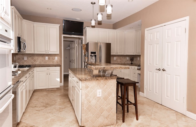 kitchen featuring white cabinets, appliances with stainless steel finishes, tasteful backsplash, decorative light fixtures, and a kitchen island