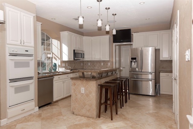 kitchen with decorative backsplash, appliances with stainless steel finishes, a kitchen island, a kitchen bar, and white cabinetry