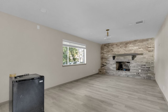 unfurnished living room featuring light hardwood / wood-style floors and a brick fireplace