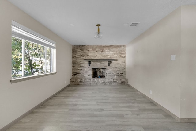 unfurnished living room featuring light wood-type flooring and a brick fireplace