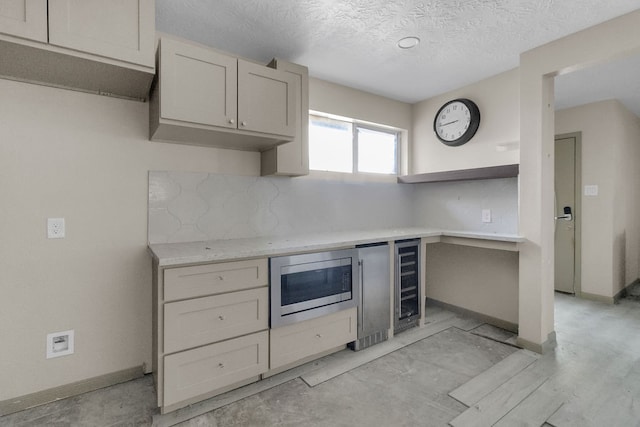 kitchen featuring backsplash, stainless steel microwave, beverage cooler, and a textured ceiling