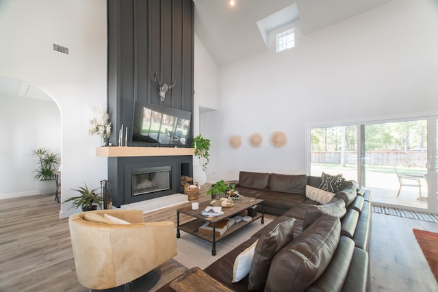 living room with a fireplace, light hardwood / wood-style flooring, high vaulted ceiling, and a healthy amount of sunlight