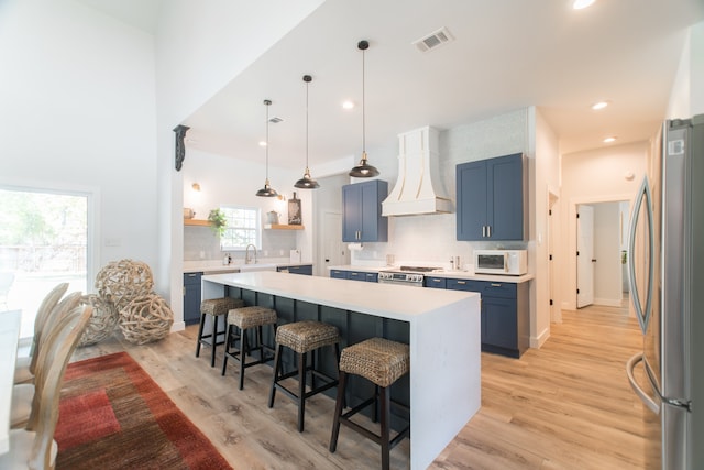 kitchen with premium range hood, light wood-type flooring, blue cabinetry, a breakfast bar area, and stainless steel appliances