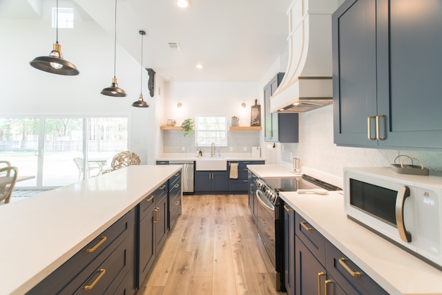 kitchen featuring appliances with stainless steel finishes, custom range hood, sink, pendant lighting, and light hardwood / wood-style flooring