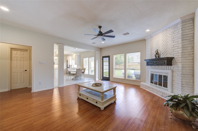 living room featuring hardwood / wood-style flooring, ceiling fan, a fireplace, a textured ceiling, and decorative columns