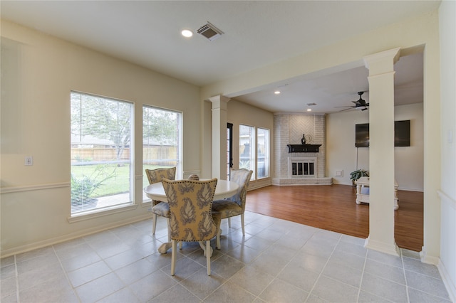 dining room with decorative columns, a brick fireplace, a wealth of natural light, and light wood-type flooring