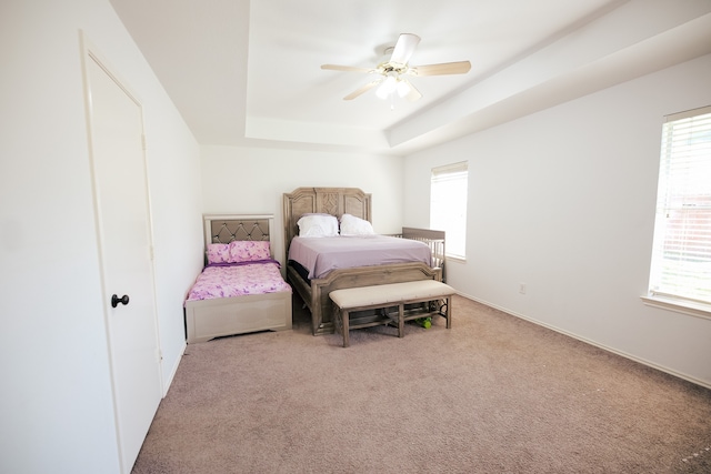 bedroom with a raised ceiling, ceiling fan, and light carpet