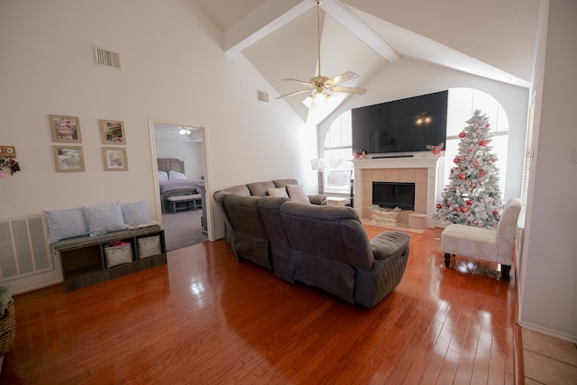 living room featuring hardwood / wood-style floors, high vaulted ceiling, ceiling fan, beam ceiling, and a tiled fireplace