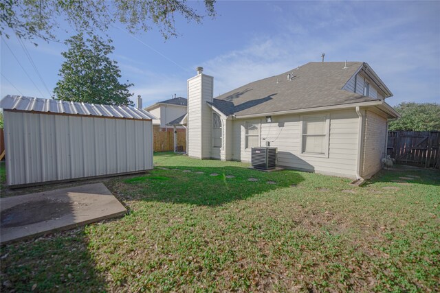 rear view of house featuring a yard, central AC unit, and a storage shed