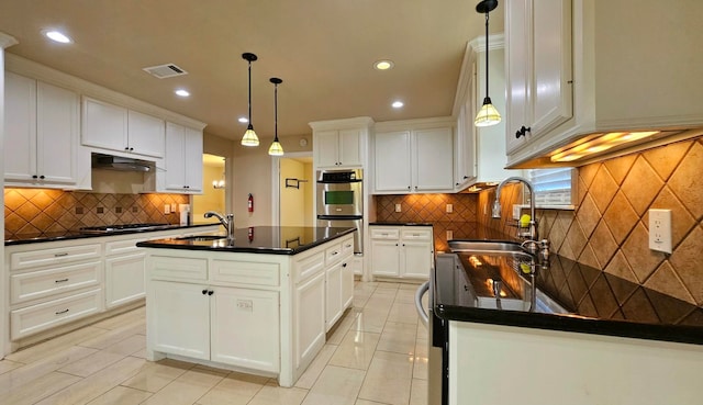 kitchen with a kitchen island with sink, sink, white cabinets, and pendant lighting