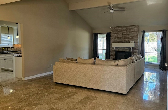 living room with lofted ceiling with beams, sink, light hardwood / wood-style flooring, a brick fireplace, and ceiling fan