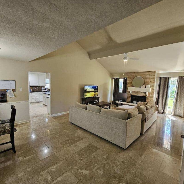 living room featuring vaulted ceiling with beams, ceiling fan, a fireplace, and a textured ceiling