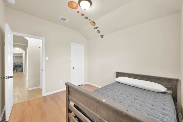 bedroom with washer / clothes dryer, vaulted ceiling, and light wood-type flooring