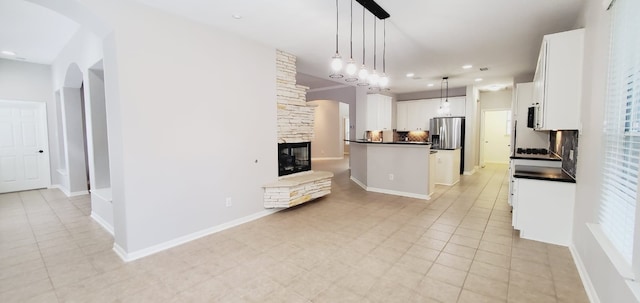 kitchen with stainless steel fridge, tasteful backsplash, pendant lighting, white cabinetry, and a stone fireplace