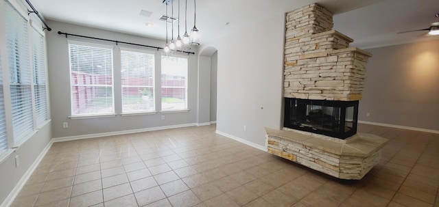 unfurnished living room with tile patterned floors, a stone fireplace, and ceiling fan