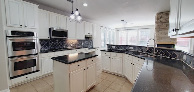 kitchen with appliances with stainless steel finishes, sink, pendant lighting, white cabinets, and a kitchen island