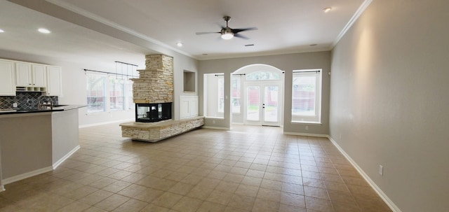 unfurnished living room with a stone fireplace, ceiling fan, crown molding, and light tile patterned floors