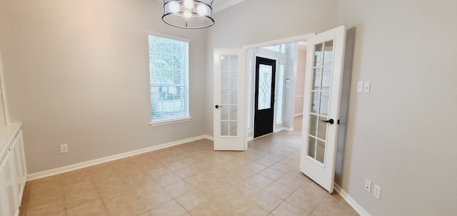 tiled empty room featuring french doors, a healthy amount of sunlight, and a notable chandelier