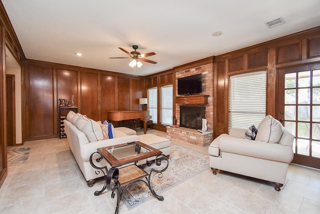 tiled living room with a fireplace, ceiling fan, and wooden walls