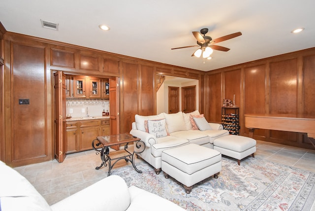 living room with ceiling fan, wood walls, and wet bar