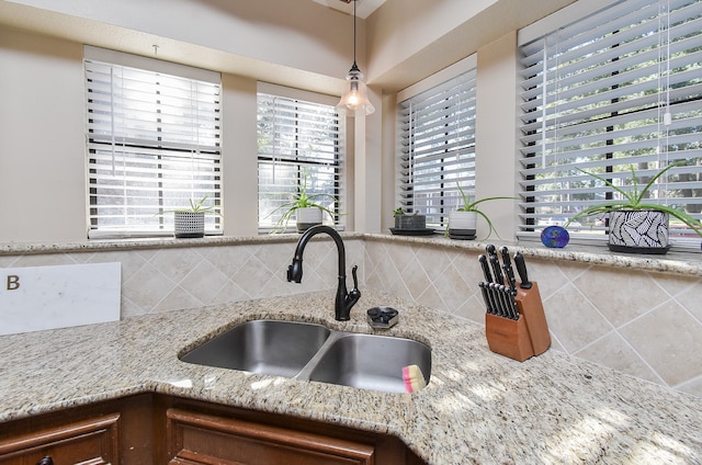 kitchen with tasteful backsplash, light stone counters, sink, and hanging light fixtures