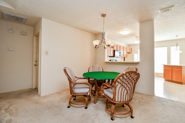 dining space with a textured ceiling, ceiling fan with notable chandelier, and light colored carpet