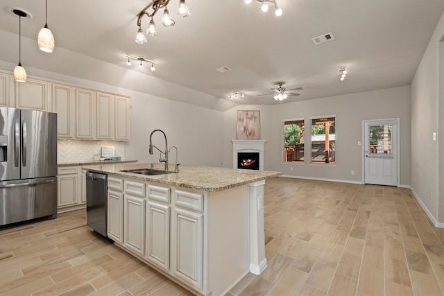 kitchen with sink, hanging light fixtures, light stone counters, a center island with sink, and appliances with stainless steel finishes