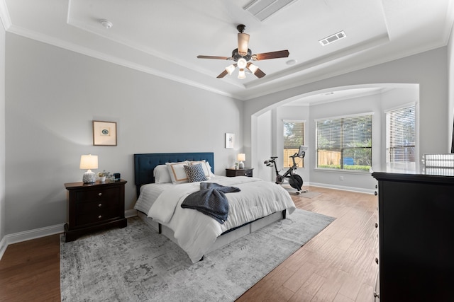 bedroom featuring hardwood / wood-style floors, a raised ceiling, ceiling fan, and ornamental molding