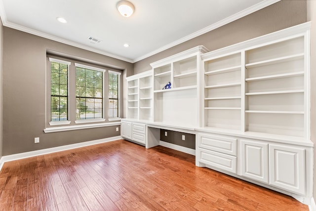 unfurnished office with light hardwood / wood-style flooring, built in desk, and ornamental molding