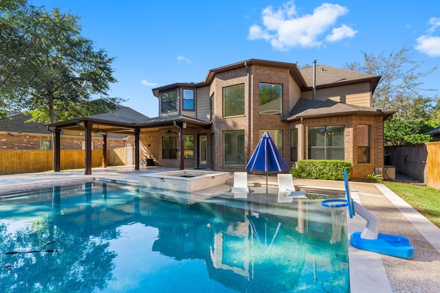 rear view of house featuring ceiling fan and a swimming pool with hot tub