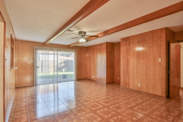 empty room with beamed ceiling, a textured ceiling, ceiling fan, and wood walls