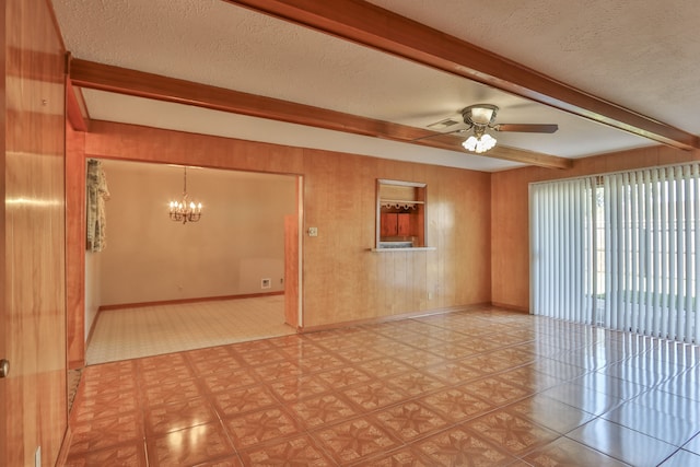 empty room featuring ceiling fan with notable chandelier, beam ceiling, a textured ceiling, and wooden walls