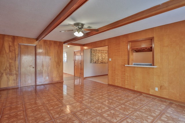 unfurnished room with beam ceiling, wood walls, ceiling fan, and a textured ceiling