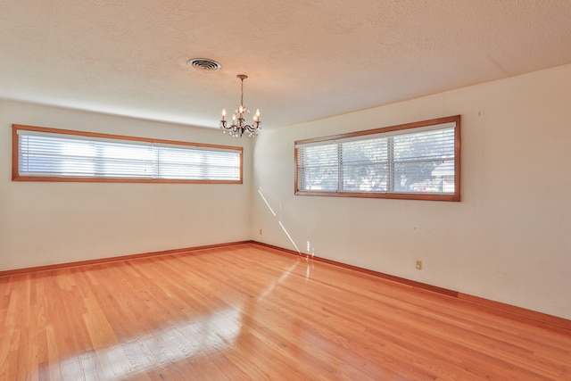 empty room with hardwood / wood-style flooring, a notable chandelier, and a wealth of natural light