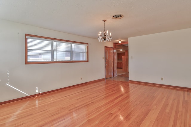 empty room with light hardwood / wood-style flooring, a textured ceiling, and a notable chandelier