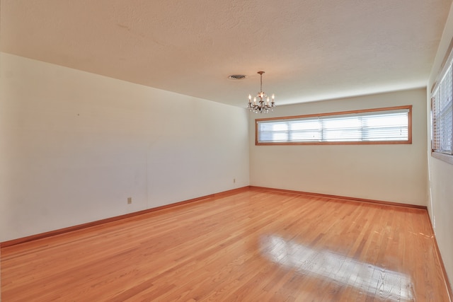 spare room with a textured ceiling, light hardwood / wood-style floors, and a notable chandelier