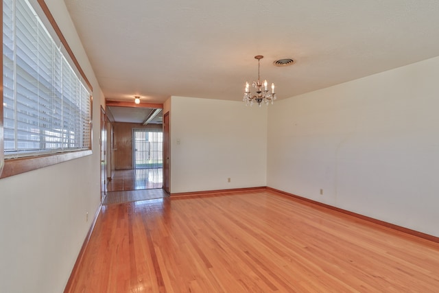 spare room featuring a chandelier and light wood-type flooring