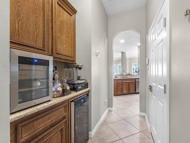 bar featuring light stone countertops, sink, wine cooler, light tile patterned flooring, and appliances with stainless steel finishes