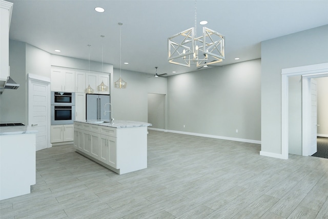 kitchen with ceiling fan with notable chandelier, stainless steel appliances, a kitchen island with sink, decorative light fixtures, and white cabinets