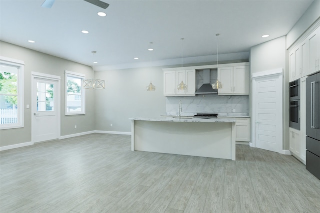 kitchen with a kitchen island with sink, white cabinetry, pendant lighting, and wall chimney range hood