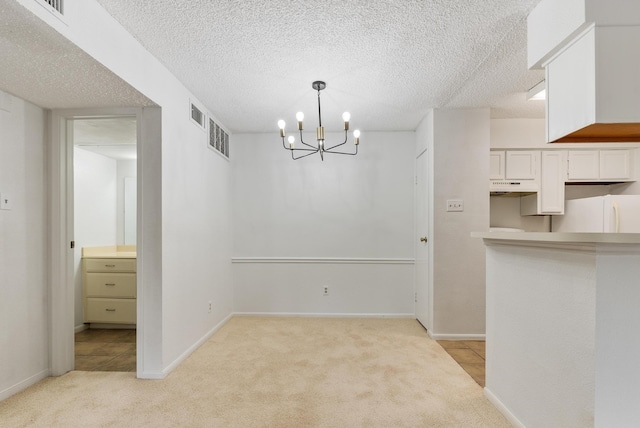 unfurnished dining area with light carpet, a chandelier, and a textured ceiling