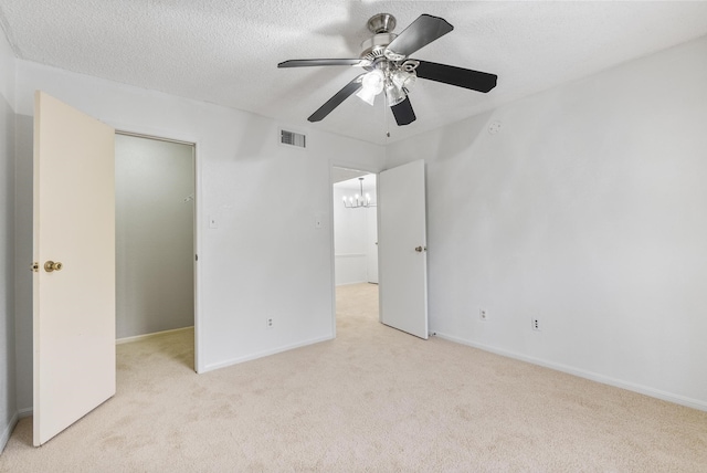 unfurnished bedroom with a textured ceiling, light carpet, a closet, and ceiling fan with notable chandelier