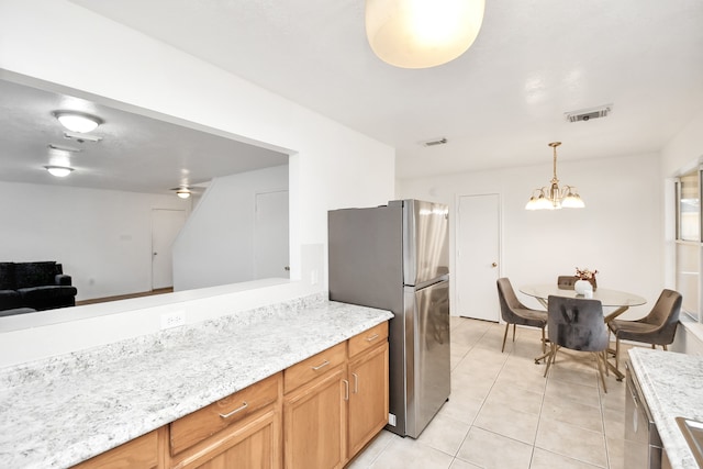 kitchen with light stone counters, stainless steel appliances, pendant lighting, an inviting chandelier, and light tile patterned flooring