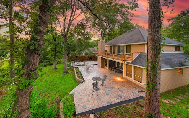 back house at dusk with a yard, a patio, and a deck