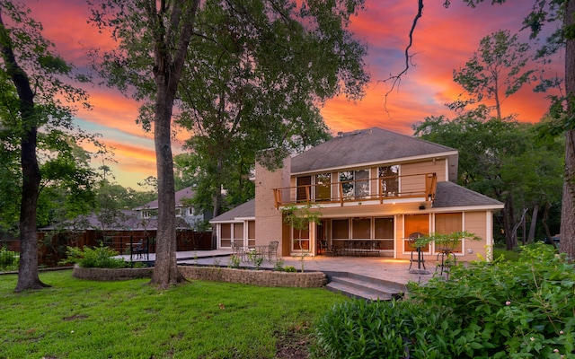 back house at dusk featuring a yard, a patio area, and a balcony